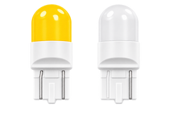 Two small LED light bulbs shown side by side on a plain white background. The left bulb has a translucent yellow top, and the right bulb has a clear/translucent white top; both have white bodies and metal contact pins at the bottom.