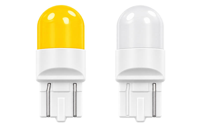 Two small LED light bulbs shown side by side on a plain white background. The left bulb has a translucent yellow top, and the right bulb has a clear/translucent white top; both have white bodies and metal contact pins at the bottom.
