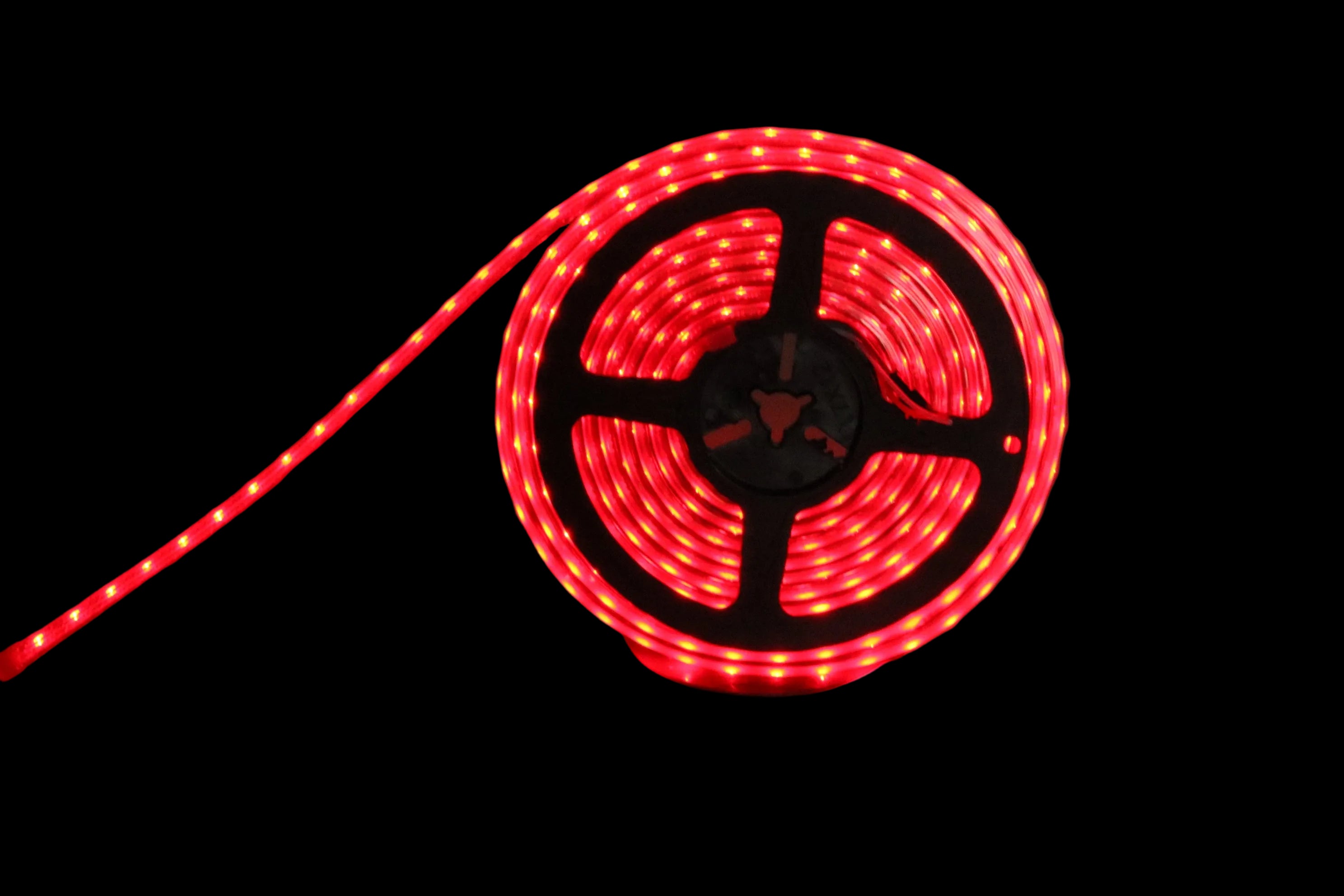 A coiled red LED light strip with a black plastic spool, photographed on a dark surface with the light glowing red.