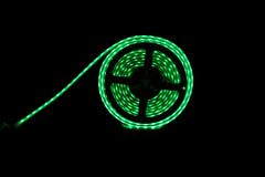 A coiled green LED light strip with a black connector core, glowing brightly against a dark background.