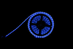 A coiled blue LED light strip with a black central hub, lying on a dark surface and casting a blue glow against a black background.