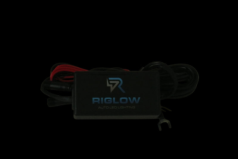 A black Biglow auto LED lighting controller box with attached black and red wires, photographed on a plain beige surface.