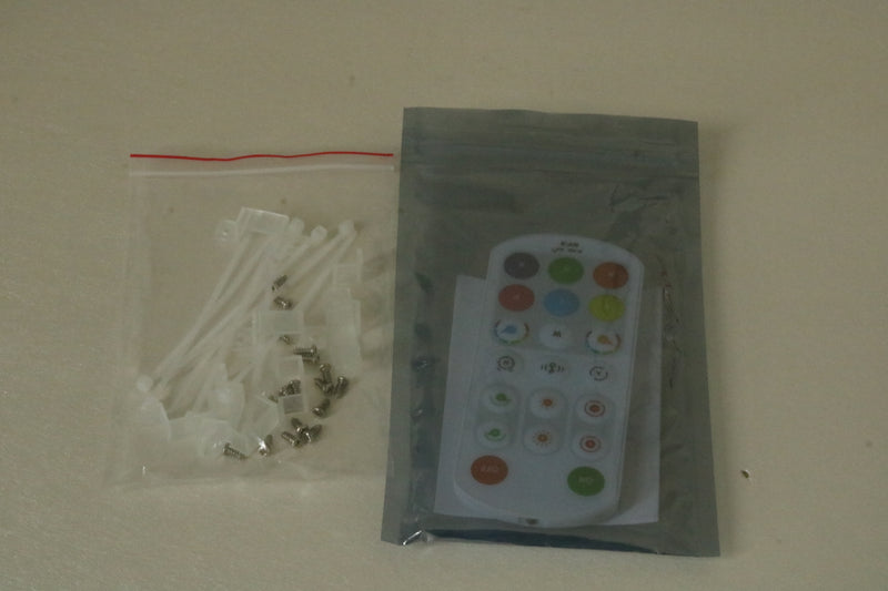 A white remote control in a clear resealable pouch next to a clear zip bag containing white plastic cable ties and small metal hardware, photographed on a plain beige surface.