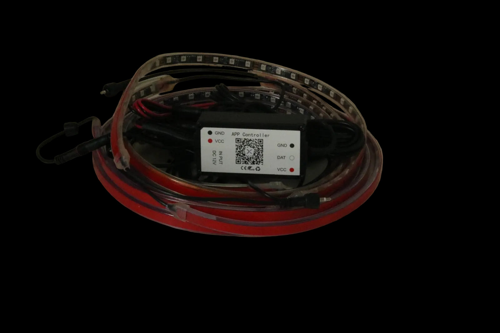 A coiled red and black LED light strip with a central black control box and a white label, photographed on a plain beige surface.